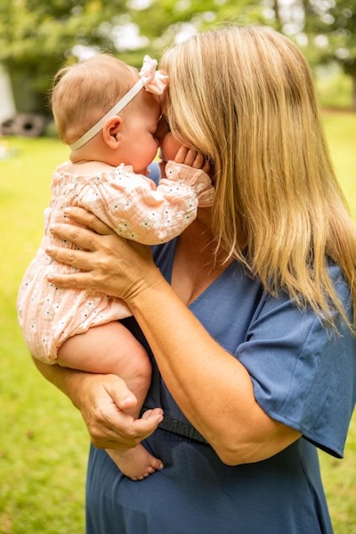A Babies & Beyond doula holding and nuzzling a smiling infant outdoors.
